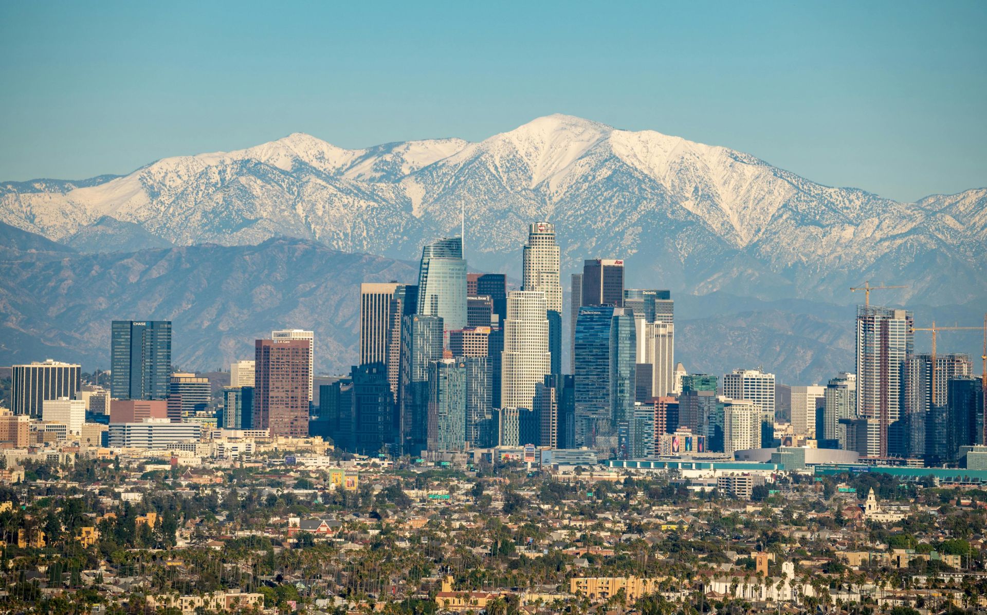 Stunning aerial view of downtown Los Angeles with snowy mountains in the background, highlighting the city skyline.