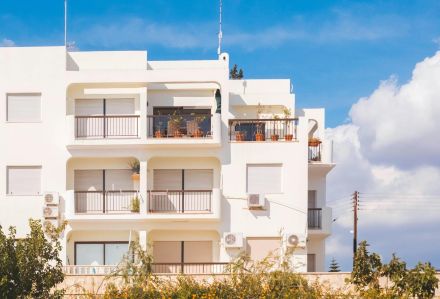 Stylish white apartment building exterior with balconies under a vibrant blue sky, showcasing modern architectural design.