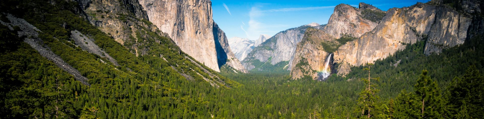 Majestic view of Yosemite Valley with lush forests, cliffs, and waterfalls under a clear blue sky.