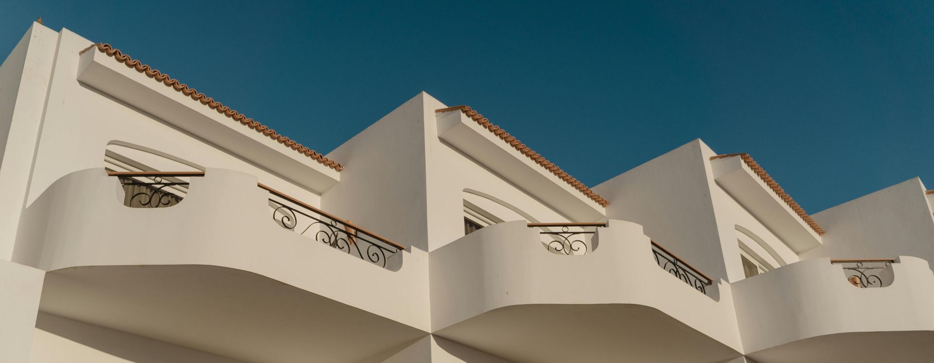 Elegant white Mediterranean building with ornate balconies under a clear blue sky.